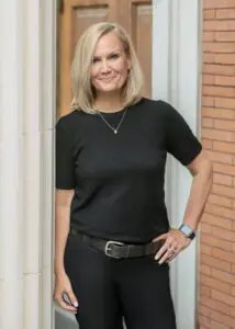 Woman in black top posing outdoors by a column.